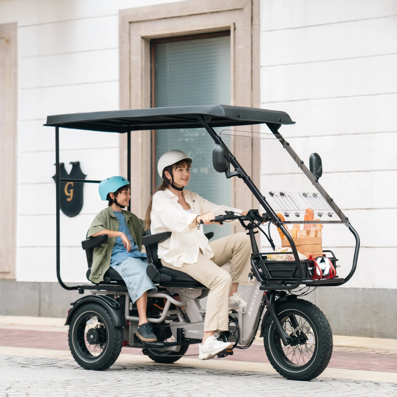 Two helmeted riders on a SERITON trike with canopy and passenger seating